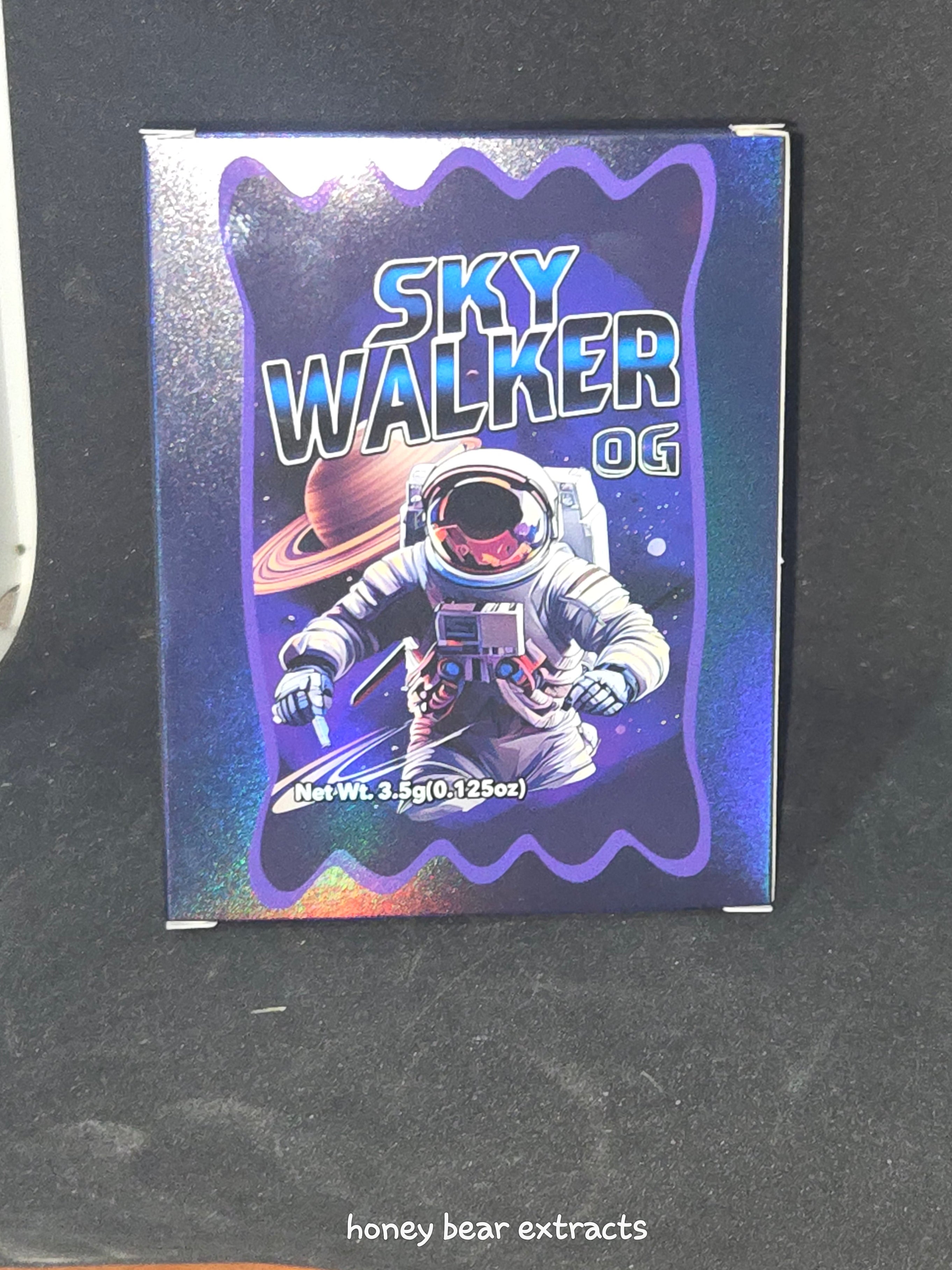 Holographic packaging of 'Sky Walker OG' by honey bear extracts on a dark background.